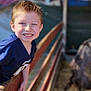 child, boy, smiling, fence, outdoor, daylight, animal_enclosure, casual_clothing, blue_shirt, short_hair, wooden_rail, happy, portrait, person, young, cheerful, daytime, animal, petting_zoo, background_blur