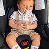 baby, infant, child, car_seat, pacifier, sitting, portrait, indoors, vehicle, seatbelt, toddler, smiling, blue_eyes, brown_hair, overalls, shoes, socks, teddy_bear, close_up, photography
