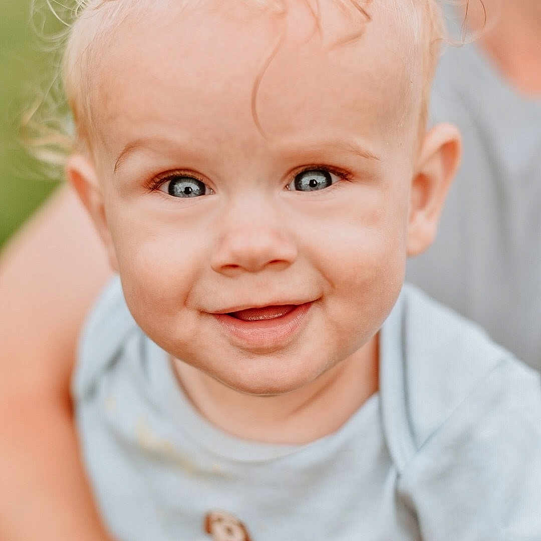 Alistir is registered to the contest to win money with this photo: baby, child, smiling, blue_eyes, blond_hair, toddler, close_up, portrait, outdoor, person, cute, happy, infant, clothing, shirt, hand, adult, face, skin, background