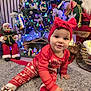 toddler, child, christmas_tree, holiday, pajamas, red_clothing, headband, bow, rug, indoor, decorations, lights, santa_claus, figurine, festive, crawling, toy, ornaments, smiling, family
