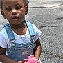 bracelet, casual_clothing, child, colorful_hair_ties, curly_hair, cute, daylight, denim_overalls, expression, holding, necklace, outdoor, pavement, person, pink_toy, playing, portrait, toddler, white_shirt, young_child