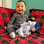 baby, child, striped_pajamas, smiling, stuffed_animal, plush_toy, couch, red_and_black, checkered_pattern, sitting, indoor, teal_wall, happy, cute, infant, furniture, cozy, home, portrait, comfort