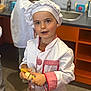Nino participe au concours pour gagner de l'argent avec cette photo : child, chef_hat, chef_uniform, kitchen_sink, toy, pretend_play, egg, counter, orange_shelves, portrait, hands, shallow_depth_of_field, play_kitchen, background_child, focused_subject, curious_expression, indoor, white_tunic, utensil, smiling
