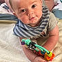 Caius is registered to the contest to win money with this photo: baby, infant, toy, blanket, bedding, striped_bib, lying_down, curious, soft_texture, child, hand, face, eyes, indoor, comfort, cute, small, play, colorful, focus