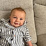 Caius is registered to the contest to win money with this photo: baby, child, smiling, striped_shirt, couch, indoor, portrait, happy, cute, face, hand, seated, clothing, infant, person, buttoned_shirt, looking_at_camera, skin, eyebrows, cheeks