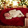 R.j is registered to the contest to win money with this photo: baby, blurred_background, child, christmas_lights, cozy, cute, decorations, festive, holiday, indoor, infant, onesie, peaceful, plush, portrait, red_blanket, sleeping, soft_lighting, toddler, warm