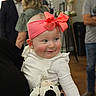 baby, child, infant, smiling, pink_bow, headband, white_outfit, stuffed_animal, cow_toy, portrait, indoor, party, people, adults, family, seated, happy, cheeks, wooden_floor, photography