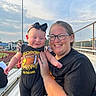 Lena joined the competition — help win amazing prizes! baby, child, mother, adult, smiling, portrait, outdoor, stadium, sports_field, bleachers, football, baseball, bow, dress, leopard_print, glasses, family, sunlight, fence, sky