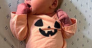 Adalynn is registered to the contest to win money with this photo: newborn, baby, infant, child, portrait, lying_down, blanket, onesie, peach_clothing, pumpkin, halloween, face, smiling, hand, fist, indoor, close_up, patterned_background, adorable, photography