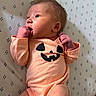 newborn, baby, infant, child, portrait, lying_down, blanket, onesie, peach_clothing, pumpkin, halloween, face, smiling, hand, fist, indoor, close_up, patterned_background, adorable, photography