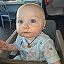 Axton is registered to the contest to win money with this photo: baby, child, high_chair, drool, necklace, blue_eyes, short_hair, shirt, indoor, diner, table, chair, person, cute, infant, seated, curious, casual, restaurant, food