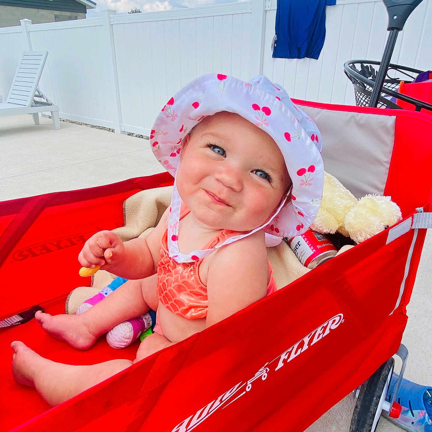 Mackenzie is registered to the contest to win money with this photo: baby, backyard, child, clothing, fence, happy, hat, outdoor, person, radio_flyer, red, seat, smiling, snack, summer, sunhat, sunny, teddy_bear, toy, wagon