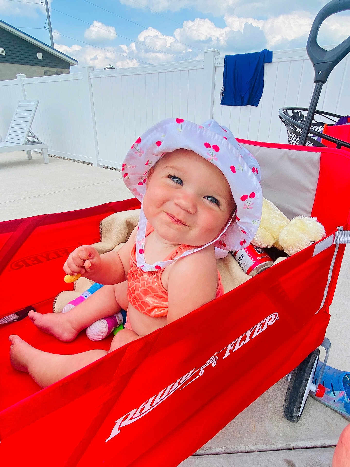 Mackenzie is registered to the contest to win money with this photo: baby, child, smiling, hat, sunhat, wagon, radio_flyer, red, outdoor, summer, backyard, fence, toy, teddy_bear, snack, clothing, sunny, happy, person, seat