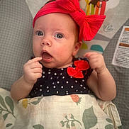 Josie is registered to the contest to win money with this photo: baby, infant, red_bow, blanket, patterned_blanket, polka_dot_clothing, monkey_illustration, baby_clothing, face, hand, indoor, cute, child, portrait, expression, newborn, headband, sitting, curious, wrapped