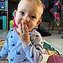 baby, child, clothing, curious, cute, dinosaur_print, eyes, face, floor, furniture, hand, home, indoor, onesie, person, playmat, shelf, sitting, toddler, toy