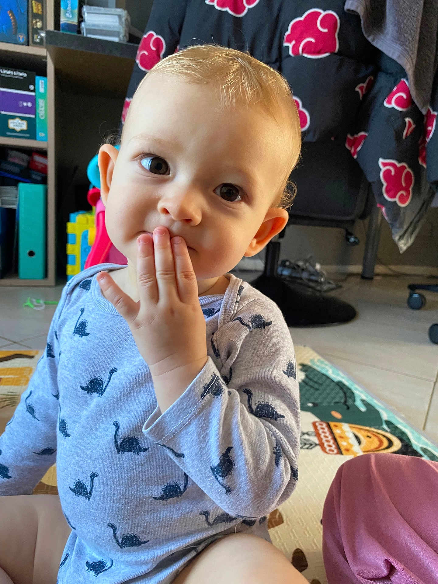 Marius a rejoint le concours — aidez-le/la à gagner de superbes lots ! baby, child, clothing, curious, cute, dinosaur_print, eyes, face, floor, furniture, hand, home, indoor, onesie, person, playmat, shelf, sitting, toddler, toy