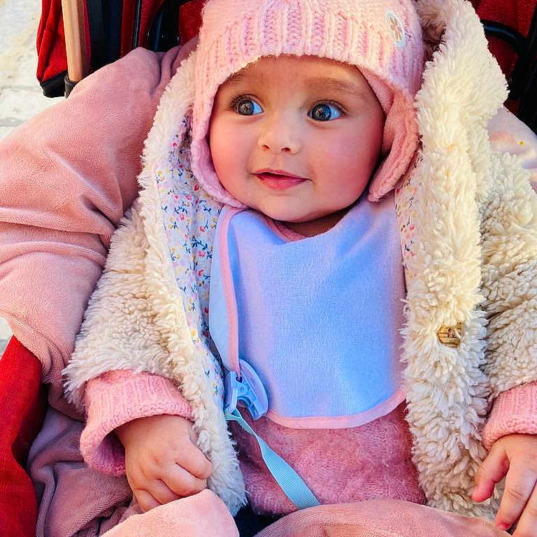 Eline a rejoint le concours — aidez-le/la à gagner de superbes lots ! baby, bib, blanket, blue_eyes, child, cozy, cute, face, hands, infant, jacket, outdoor, pink_hat, portrait, seated, smile, soft_texture, stroller, warm, winter_clothing