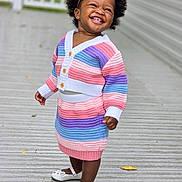 Oluwatise is registered to the contest to win money with this photo: toddler, child, smiling, happy, outdoor, knitwear, striped_clothing, headband, flower, white_shoes, wooden_deck, fence, portrait, cute, fashion, person, standing, daylight, feet, joyful