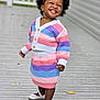 toddler, child, smiling, happy, outdoor, knitwear, striped_clothing, headband, flower, white_shoes, wooden_deck, fence, portrait, cute, fashion, person, standing, daylight, feet, joyful