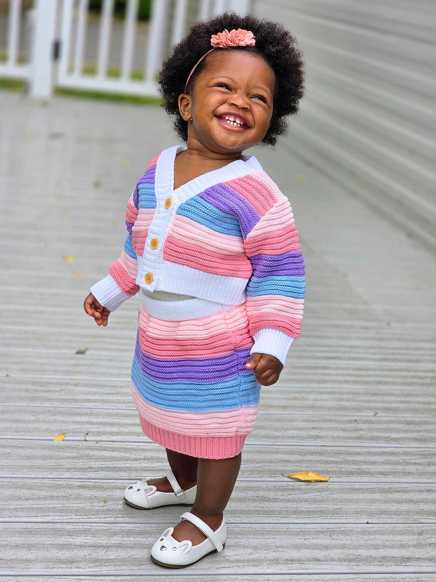 Oluwatise is registered to the contest to win money with this photo: toddler, child, smiling, happy, outdoor, knitwear, striped_clothing, headband, flower, white_shoes, wooden_deck, fence, portrait, cute, fashion, person, standing, daylight, feet, joyful