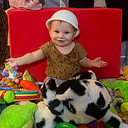 Grayson joined the competition — help win amazing prizes! baby, child, toy, stuffed_animal, plush, red_cushion, green_toy, indoor, playtime, smiling, hat, person, floor, colorful, infant, cute, happy, toddler, clothing, playroom