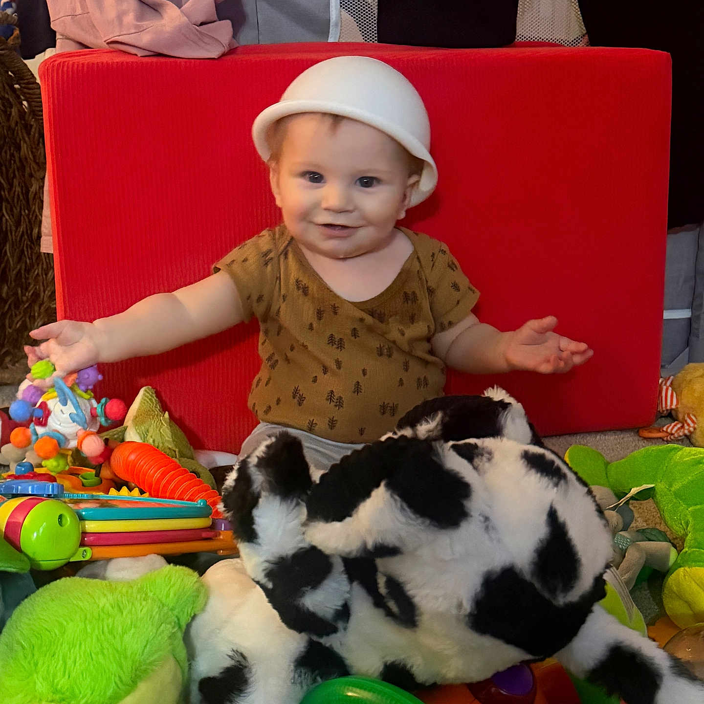 Grayson joined the competition — help win amazing prizes! baby, child, toy, stuffed_animal, plush, red_cushion, green_toy, indoor, playtime, smiling, hat, person, floor, colorful, infant, cute, happy, toddler, clothing, playroom