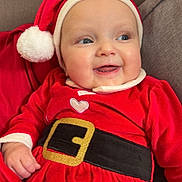 Leyah a rejoint le concours — aidez-le/la à gagner de superbes lots ! baby, child, smiling, santa_hat, christmas_outfit, red_clothing, holiday, couch, indoor, cute, portrait, festive, happy, infant, plush, seat, cozy, face, person, cheerful