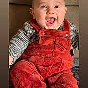 Sacha a rejoint le concours — aidez-le/la à gagner de superbes lots ! baby, infant, smiling, laughing, mouth_open, face, eyes, ears, red_overalls, corduroy, plaid_shirt, sitting, couch, cozy, chubby_cheeks, portrait, hands, legs, blanket, indoor