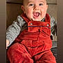 baby, infant, smiling, laughing, mouth_open, face, eyes, ears, red_overalls, corduroy, plaid_shirt, sitting, couch, cozy, chubby_cheeks, portrait, hands, legs, blanket, indoor