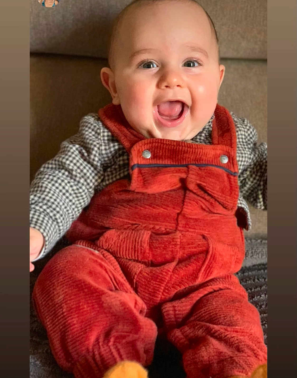 Sacha a rejoint le concours — aidez-le/la à gagner de superbes lots ! baby, infant, smiling, laughing, mouth_open, face, eyes, ears, red_overalls, corduroy, plaid_shirt, sitting, couch, cozy, chubby_cheeks, portrait, hands, legs, blanket, indoor
