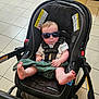 Ryder is registered to the contest to win money with this photo: baby, sunglasses, car_seat, stroller, child, infant, blanket, floor, tile, warning_sign, footwear, toddler, indoor, seatbelt, clothing, cute, person, baby_boy, casual, relaxed