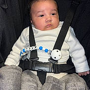 Maël a rejoint le concours — aidez-le/la à gagner de superbes lots ! baby, infant, car_seat, blanket, clothing, pacifier_clip, black_straps, white_sweater, child, face, person, indoor, cute, seat_belt, baby_accessory, toddler, portrait, resting, secure, soft