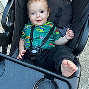 Jayce joined the competition — help win amazing prizes! baby, child, smile, stroller, seatbelt, foot, green_shirt, cartoon_print, outdoor, happy, person, clothing, black_pants, hand, face, head, hair, toy_cart, seat, playful