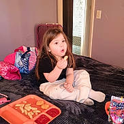 Ashley is registered to the contest to win money with this photo: child, kid, food, fries, chicken_nuggets, ketchup, tray, bed, blanket, sitting, snack, long_hair, clothing, white_pants, black_shirt, indoor, purple_wall, bag, door, juice_pouch