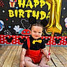 Jesus is registered to the contest to win money with this photo: baby, birthday, child, toddler, portrait, sitting, smiling, face, balloon, number_one, golden_balloon, party, celebration, costume, bow_tie, red_clothing, black_clothing, mouse_ears, birthday_backdrop, wooden_floor