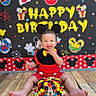baby, child, birthday, birthday_cake, mickey_mouse, disney_theme, costume, smiling, happy, sitting, portrait, party, cake, colorful, indoor, backdrop, wooden_floor, celebration, frosting, baby_food
