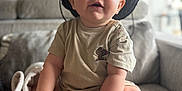 Ezio participe au concours pour gagner de l'argent avec cette photo : baby, child, hat, blue_eyes, beige_clothing, cactus_patch, sitting, couch, gray_couch, indoors, living_room, curious, happy, cute, portrait, infant, cozy, smiling, hands, feet