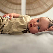 Ezio participe au concours pour gagner de l'argent avec cette photo : baby, child, blue_eyes, lying_down, beige_clothing, soft_surface, closeup, portrait, curious, indoor, cute, face, skin, hair, infant, young_child, resting, peaceful, expression, warm_lighting