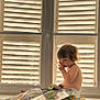 toddler, child, baby, book, window, shutters, pacifier, indoor, sunlight, curly_hair, sitting, reading, diaper, home, couch, window_handle, daylight, cute, curious, relaxed