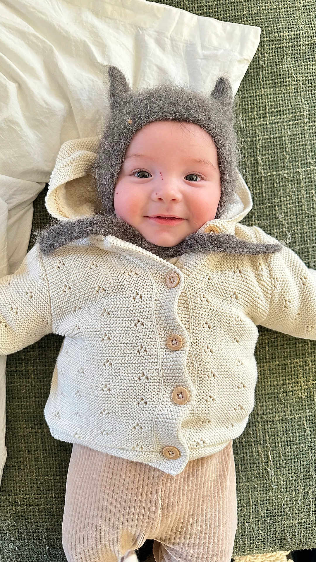 Raoul a rejoint le concours — aidez-le/la à gagner de superbes lots ! baby, child, smiling, knit_sweater, hat, cozy, ears, lying_down, green_background, pillow, cute, infant, warm_clothing, buttoned_sweater, soft_texture, face, headwear, portrait, indoors, happy