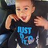 basketball_graphic, black_tshirt, car_interior, car_seat, child, daylight, excited, face, hands_up, happy, indoors, person, seat, seatbelt, shorts, smiling, text_on_clothing, toddler, window, young_child