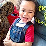 adult, candid, casual_clothing, chair, child, curly_hair, cute, denim_overalls, furniture, happy, home, indoor, living_room, person, portrait, red_shirt, seated, smiling, sofa, toddler