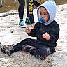 black_clothing, casual, child, curious, cute, daylight, green_sneakers, hoodie, nature, outdoor, pacifier, person, playing, river, sand, shoes, sitting, toddler, water, young_child