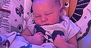 Donovan is registered to the contest to win money with this photo: newborn, baby, sleeping, infant, portrait, close_up, baby_seat, lion, blanket, toy, clothing, indoors, colorful, purple_lighting, relaxed, peaceful, sitting, nursery, patterned_fabric, face