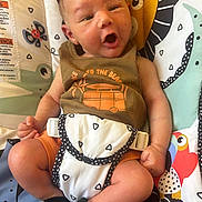 Donovan joined the competition — help win amazing prizes! newborn, baby, infant, child, portrait, yawning, sitting, baby_seat, harness, blanket, colorful, patterned, animal_print, playroom, indoor, cozy, clothing, orange_shorts, facial_expression, photography