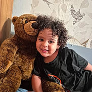 Aylon participe au concours pour gagner de l'argent avec cette photo : child, teddy_bear, curly_hair, black_tshirt, smiling, plush_toy, indoors, wallpaper, bird_pattern, leaf_pattern, bed, pillow, happy, portrait, person, soft_toy, cozy, cute, young_child, home