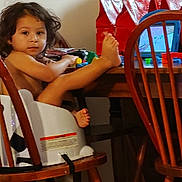 Marcelo joined the competition — help win amazing prizes! toddler, child, high_chair, table, wooden_chair, toys, red_gift_bags, indoor, curly_hair, barefoot, face, person, furniture, playing, young_child, legs, looking, home, casual, relaxed