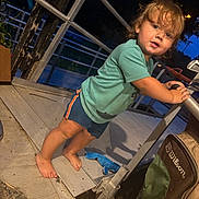 Billy G is registered to the contest to win money with this photo: toddler, child, outdoor, evening, portrait, standing, curious, face, eyes, hair, smiling, green_shirt, shorts, barefoot, stroller, patio, deck, railing, night, candid