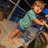 toddler, child, outdoor, evening, portrait, standing, curious, face, eyes, hair, smiling, green_shirt, shorts, barefoot, stroller, patio, deck, railing, night, candid