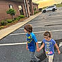 child, children, boy, girl, holding_hands, parking_lot, sidewalk, building, brick_wall, car, sunset, outdoor, casual_clothing, asphalt, curb, side_view, young, walking, daylight, nature